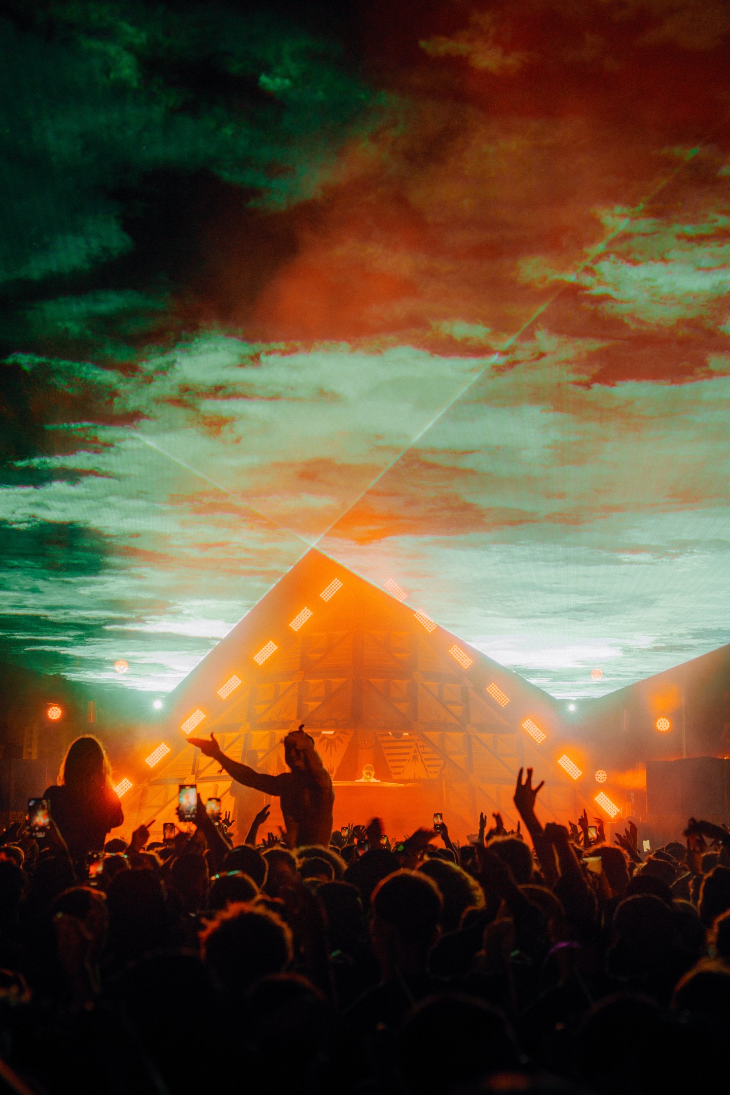 Laser lit pyramid stage and crowd inside a venue at night
