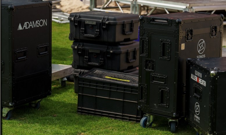 Flight cases of sound and lighting kit lined up on the grass at a Phuket festival site before the build