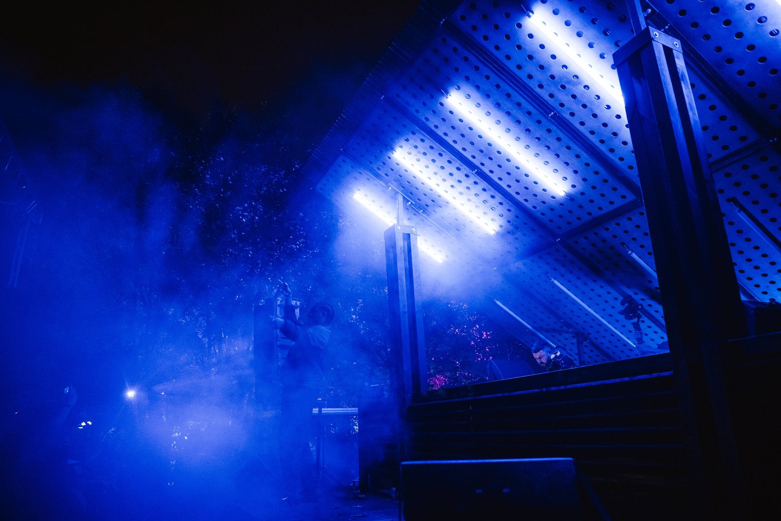 Stage structure lit blue with smoke drifting through the trees at night