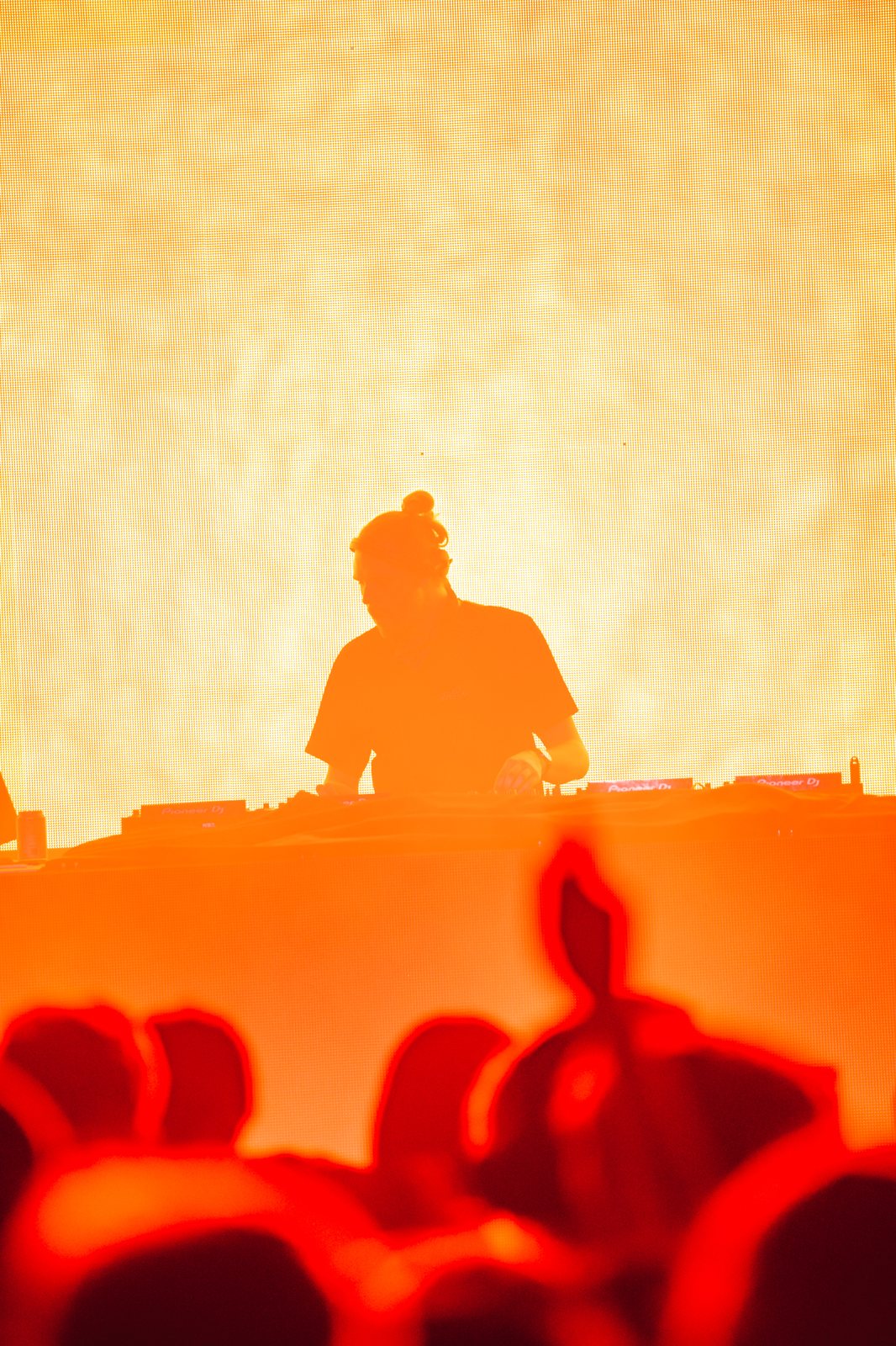 DJ silhouetted against an orange wall of light with the crowd in front