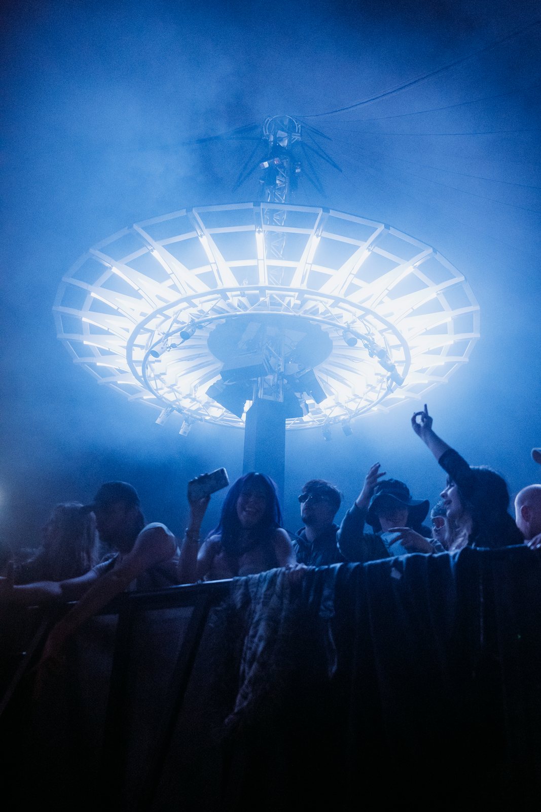 Crowd at the barrier under a circular lighting rig in blue smoke