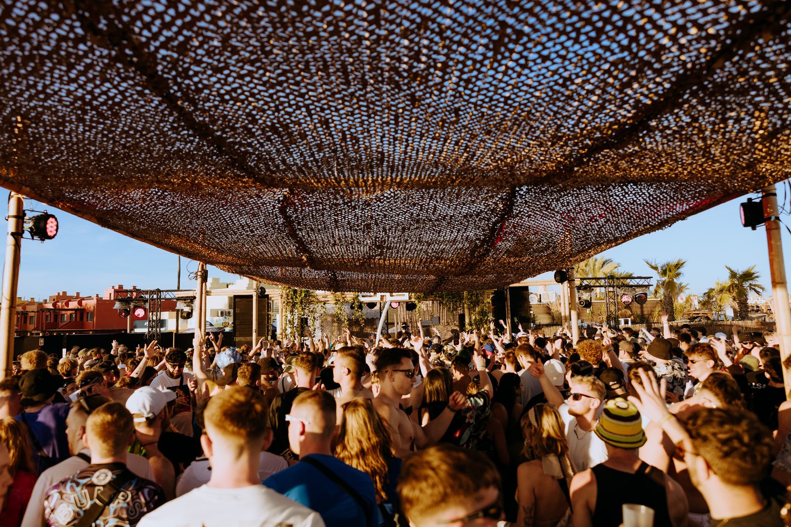 Crowd dancing under a camouflage net shade in the afternoon sun